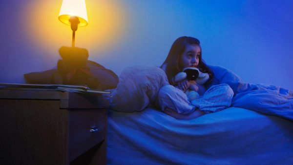 Девочка сидит на кровати под одеялом при ночнике