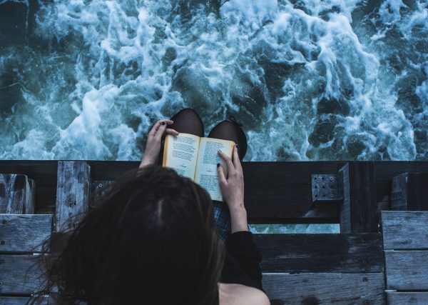 Девушка читает книгу в одиночестве у реки
