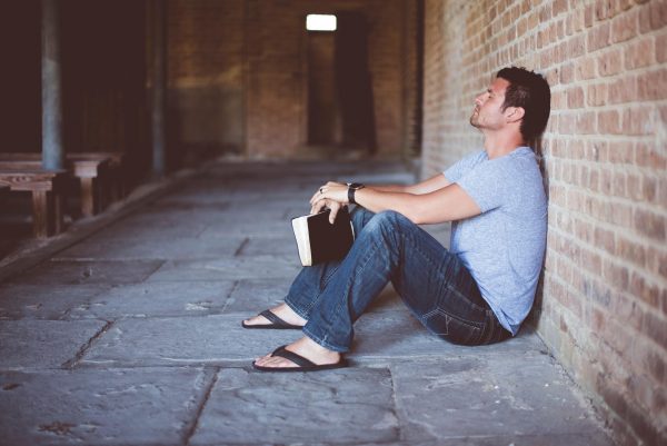 Мужчина с книгой сидит на полу у стены