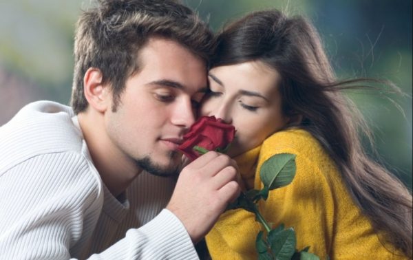 Юные возлюбленные, прильнувшие щекой к щеке, вдыхают аромат алой розы