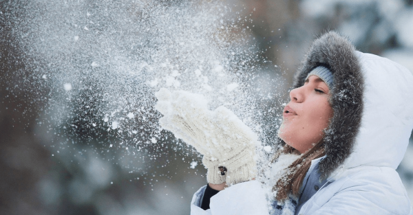 Девушка зимой дует на ладони со снегом
